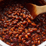 Delicious baked beans with crispy bacon on top, served in a rustic bowl, highlighting the ingredients like BBQ sauce and spices.