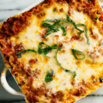 Sliced vegetable lasagna with bell peppers, zucchini, and cheese, topped with fresh basil leaves.