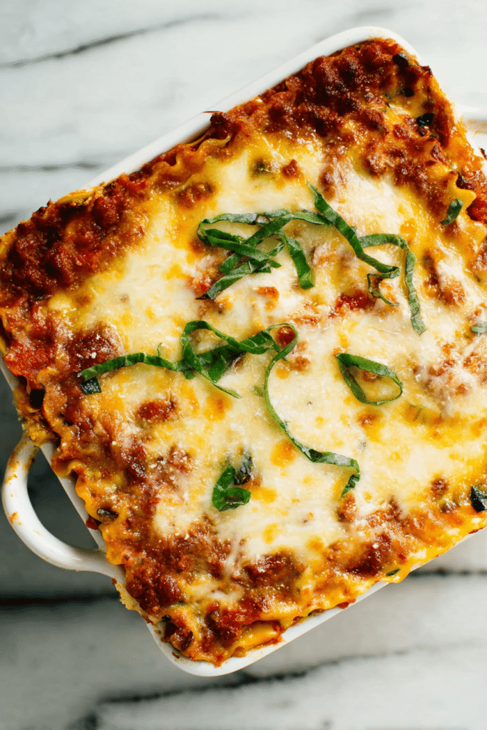 Sliced vegetable lasagna with bell peppers, zucchini, and cheese, topped with fresh basil leaves.