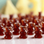 Colorful black elderberry gummies shaped like bears, surrounded by fresh elderberries on a wooden table.