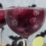 Black magic margarita with blackberries and mint leaves on a tropical background.