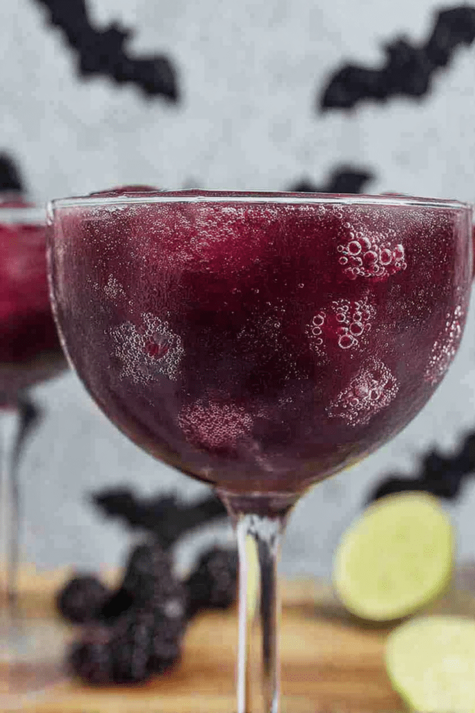 Black magic margarita with blackberries and mint leaves on a tropical background.