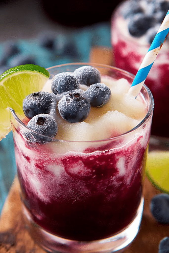 Refreshing boozy blueberry limeade slushie in a glass with lime wedges and blueberries on a vibrant summer background.
