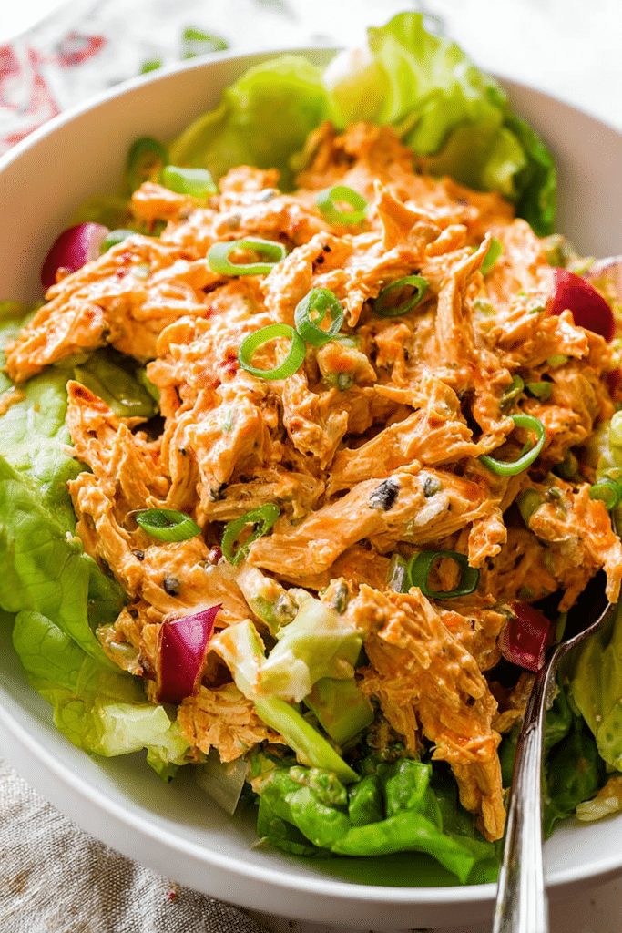 Bowl of buffalo chicken salad garnished with green onions and blue cheese crumbles on a wooden table