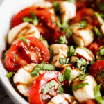 Delicious Caprese salad with cherry tomatoes, mozzarella balls, and fresh basil on a wooden table.