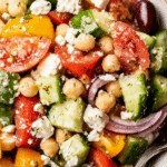 Chickpea Greek salad with bell peppers, tomatoes, olives, and feta cheese in a large bowl.