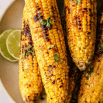 Chili lime grilled corn on the cob topped with chili butter, lime wedges, and cilantro.