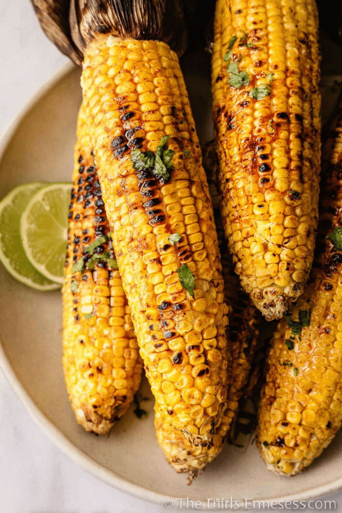 Chili lime grilled corn on the cob topped with chili butter, lime wedges, and cilantro.