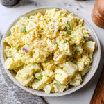 A colorful bowl of classic potato salad garnished with herbs on a picnic table.