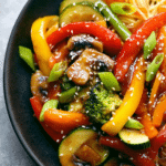Colorful vegetable stir fry in a wok with bell peppers, broccoli, and carrots, topped with sesame seeds.