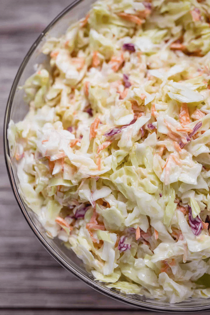 Close-up of freshly made coleslaw in a rustic bowl, featuring shredded cabbage and carrots, perfect for summer barbecues.