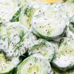 Creamy cucumber dill salad in a bowl with fresh dill and lemon slices on a wooden table