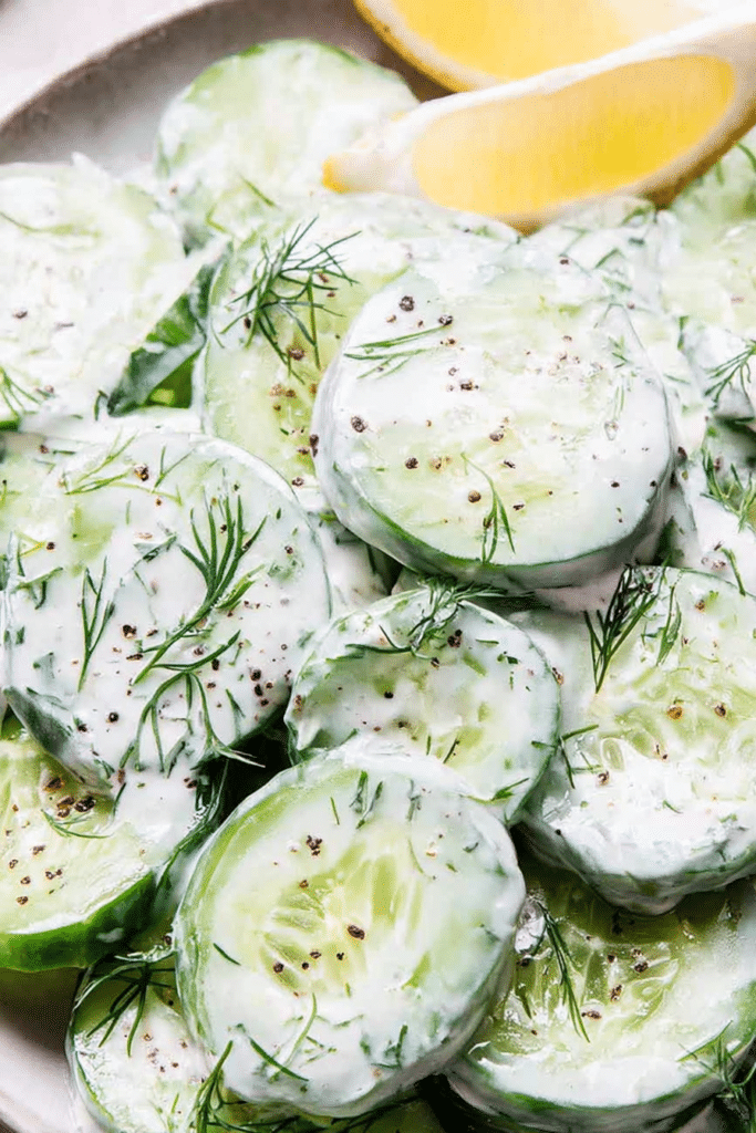 Creamy cucumber dill salad in a bowl with fresh dill and lemon slices on a wooden table