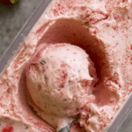 Close-up of creamy homemade strawberry ice cream topped with fresh strawberries and mint leaves, ideal for summer desserts.