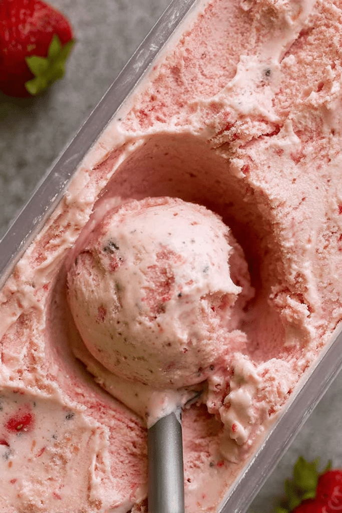 Close-up of creamy homemade strawberry ice cream topped with fresh strawberries and mint leaves, ideal for summer desserts.