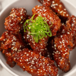 Crispy Korean gochujang honey wings garnished with sesame seeds and green onions on a wooden platter