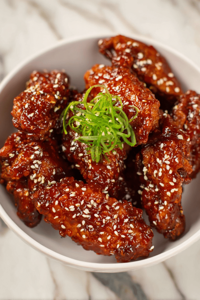 Crispy Korean gochujang honey wings garnished with sesame seeds and green onions on a wooden platter