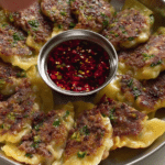 Crispy smashed gyozas on a plate with chili oil and scallions, highlighting the delicious filling and golden-brown wonton wrappers.