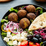 Delicious easy falafel salad bowl with greens, tomatoes, falafels, feta, and mustard hummus.