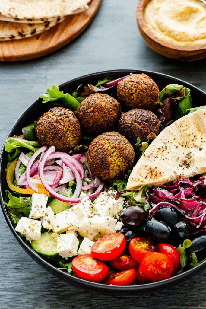 Delicious easy falafel salad bowl with greens, tomatoes, falafels, feta, and mustard hummus.