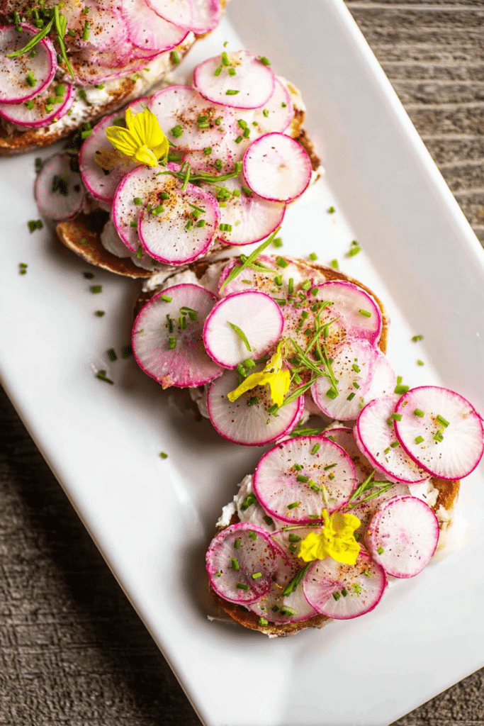 A plate of easy French buttered radish toasts topped with sliced radishes, chives, and edible flowers, ideal as an appetizer.