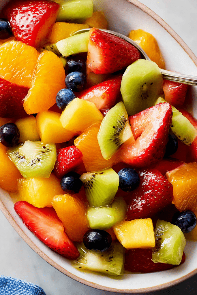 Bright and colorful fruit salad with strawberries, blueberries, kiwi, and mandarin oranges in a bowl.