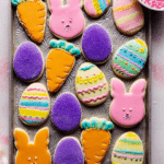 Festively decorated Easter cookies in the shape of eggs, bunnies, and carrots with vibrant icing and sprinkles on a decorative platter.