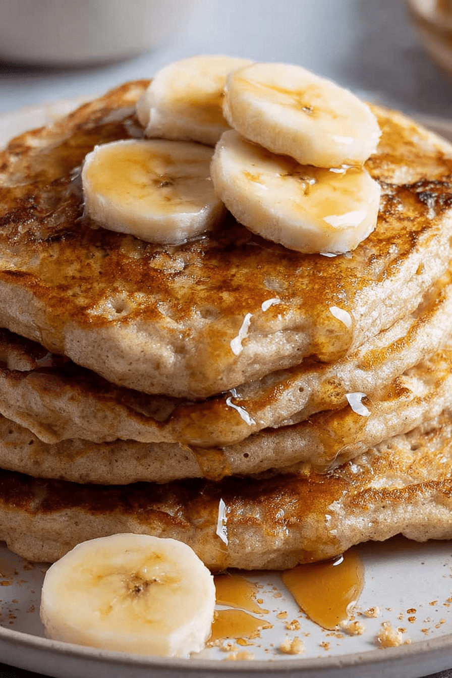 Fluffy banana pancakes stacked high with banana slices and maple syrup on a rustic table