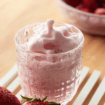 Tall glass of fluffy strawberry cold foam topped with fresh strawberries and mint on a wooden table.