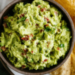 Freshly made guacamole in a bowl with tortilla chips, cilantro, and lime slices on a rustic wooden table.