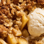 Delicious freshly baked apple crumble with a golden crust and vanilla ice cream on top.