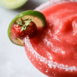 Vibrant frozen strawberry margarita cocktail with fresh strawberries and lime slice garnishes on a sunny patio