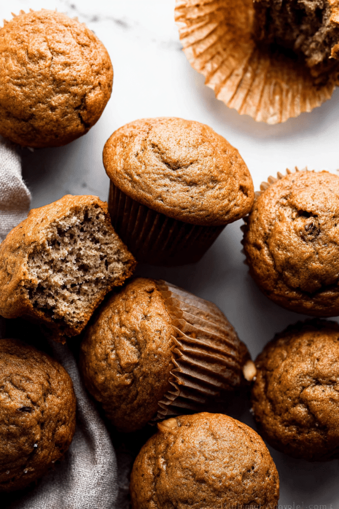 Delicious golden-brown banana muffins with melted butter and cinnamon on a wooden table, surrounded by fresh bananas and walnuts.
