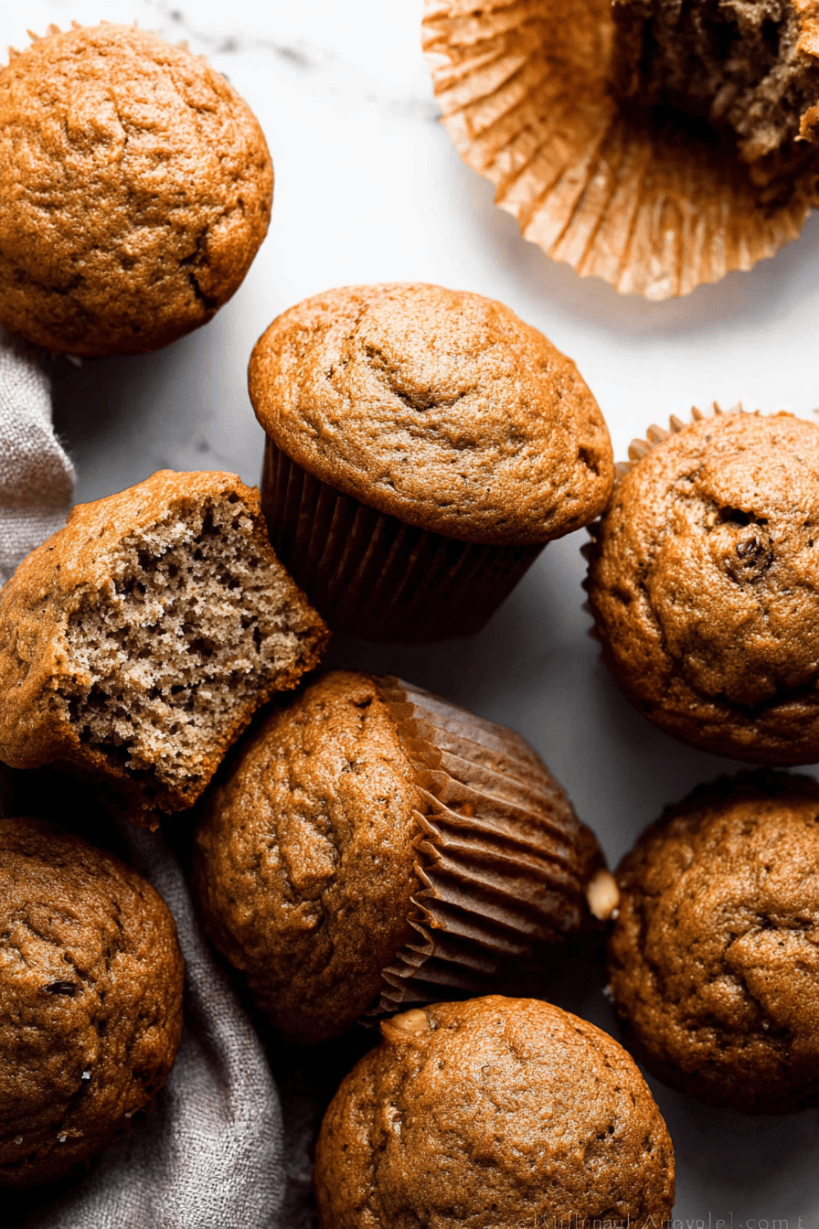 Delicious golden-brown banana muffins with melted butter and cinnamon on a wooden table, surrounded by fresh bananas and walnuts.