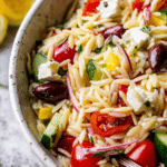 Fresh and colorful Greek Orzo Salad served in a bowl with vegetables, feta cheese, and herbs, perfect for summer meals.