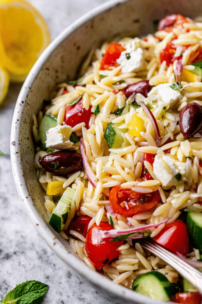 Fresh and colorful Greek Orzo Salad served in a bowl with vegetables, feta cheese, and herbs, perfect for summer meals.