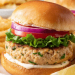 Grilled ground chicken burger garnished with fresh lettuce, tomato, and red onions on a wooden table.