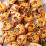 Delicious grilled shrimp skewers with parsley and lemon slices on a wooden platter.