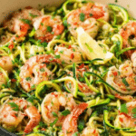 Healthy shrimp scampi with zucchini noodles garnished with parsley and lemon on a white plate