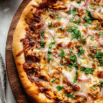 Close-up of homemade BBQ chicken pizza with cilantro, red onion, and melted cheese on a wooden board.