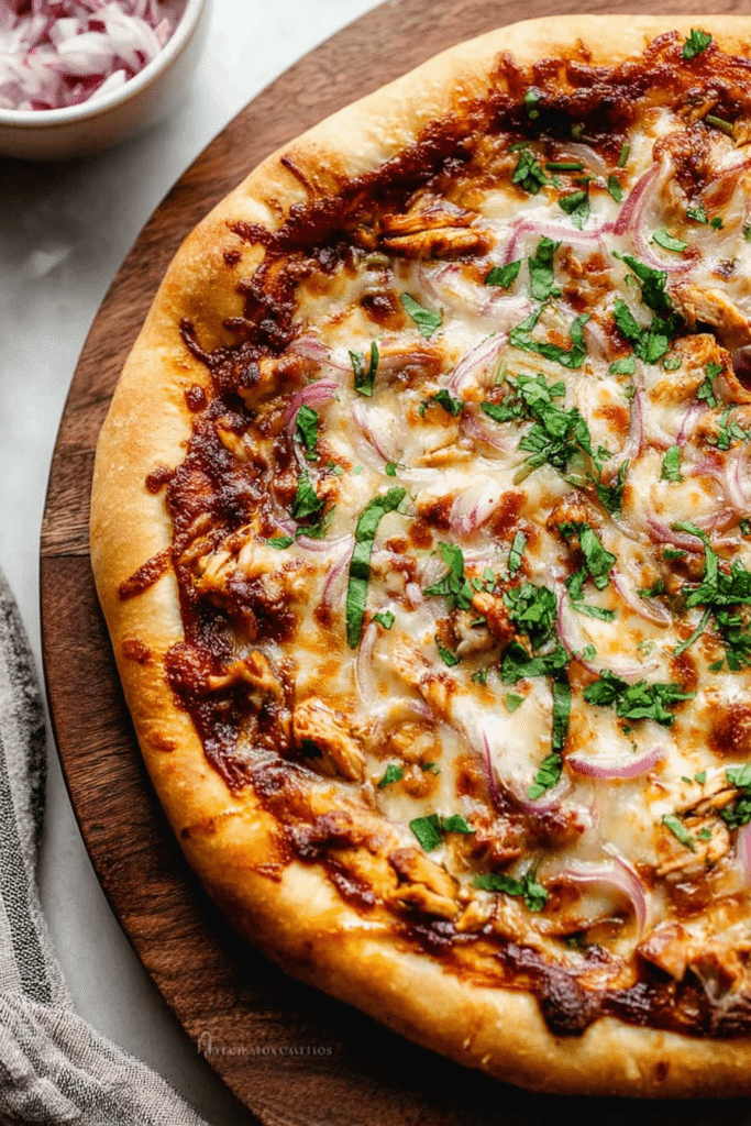 Close-up of homemade BBQ chicken pizza with cilantro, red onion, and melted cheese on a wooden board.