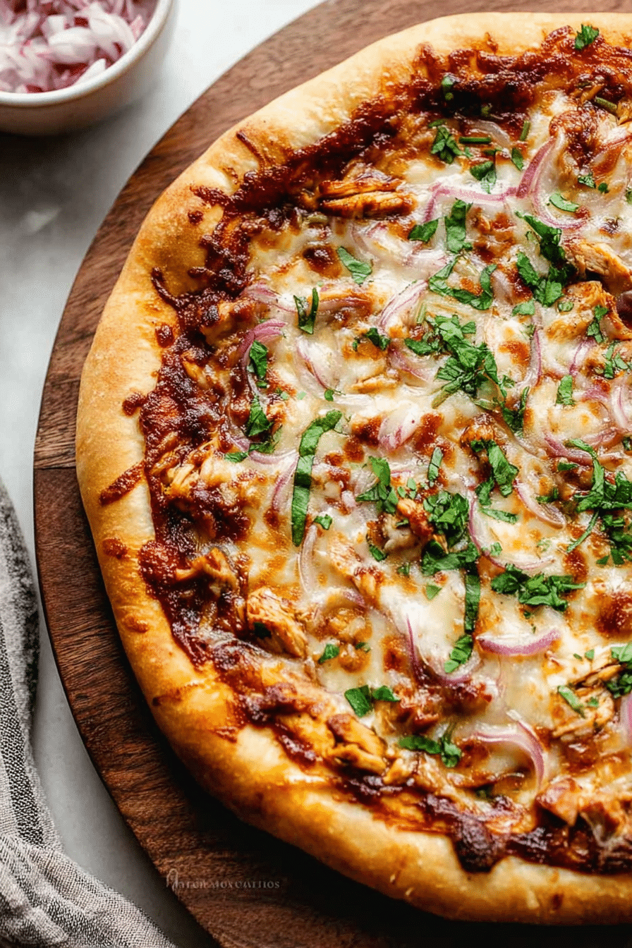 Close-up of homemade BBQ chicken pizza with cilantro, red onion, and melted cheese on a wooden board.