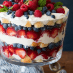 Close-up of a colorful berry trifle with layers of strawberries, blueberries, and whipped cream in a glass dish.