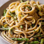 Delicious lemon asparagus pasta with fresh herbs on a white plate, garnished with lemon slices.