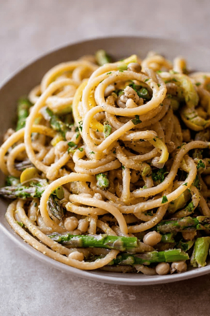 Delicious lemon asparagus pasta with fresh herbs on a white plate, garnished with lemon slices.