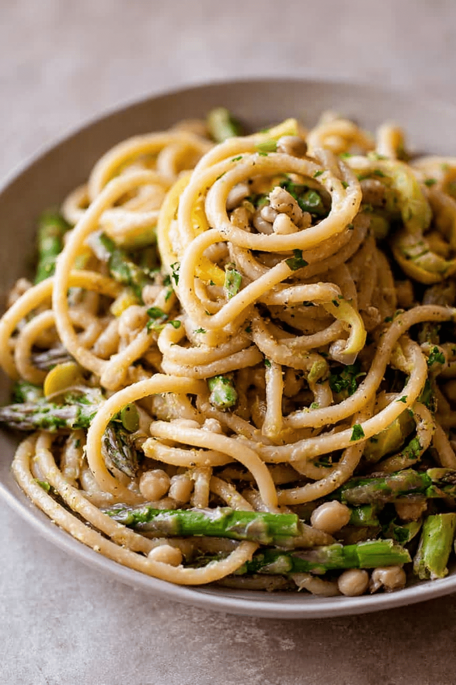 Delicious lemon asparagus pasta with fresh herbs on a white plate, garnished with lemon slices.