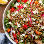 Lemon balsamic lentil salad with spinach, bell pepper, cucumber, and feta cheese served in a bowl with a lemon wedge