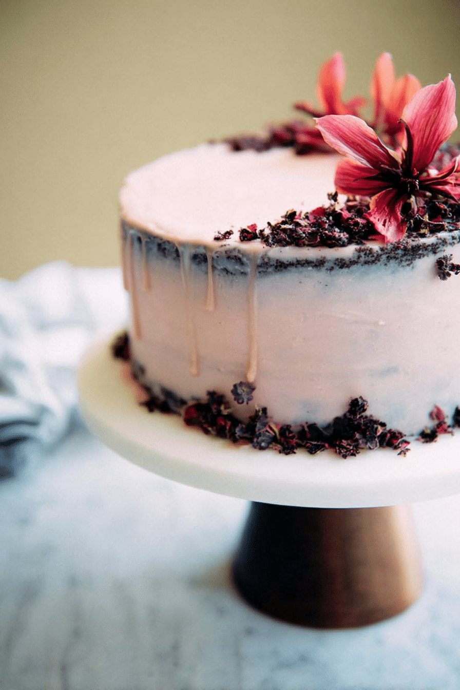 A stunning naked hibiscus chocolate cake decorated with fresh hibiscus flowers, showcasing its rich chocolate layers and smooth frosting.