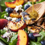 Delicious peach salad with grilled peaches, spinach, blueberries, goat cheese, and pecans on a wooden table.