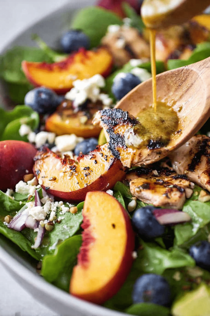 Delicious peach salad with grilled peaches, spinach, blueberries, goat cheese, and pecans on a wooden table.